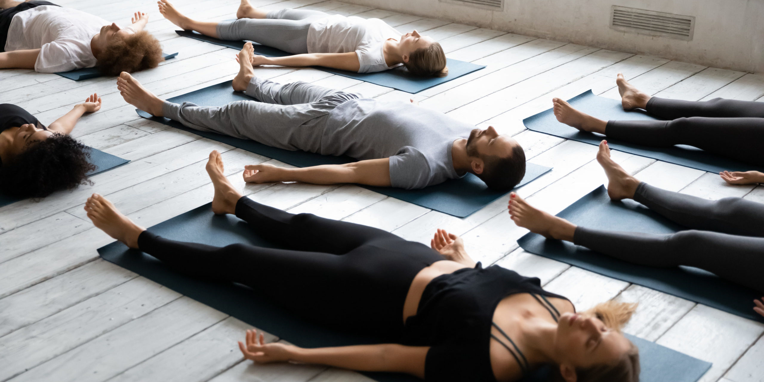 Group of young people with closed eyes meditating in Savasana pose on the floor in Salt Lake City, UT | Santosh Yoga Institute