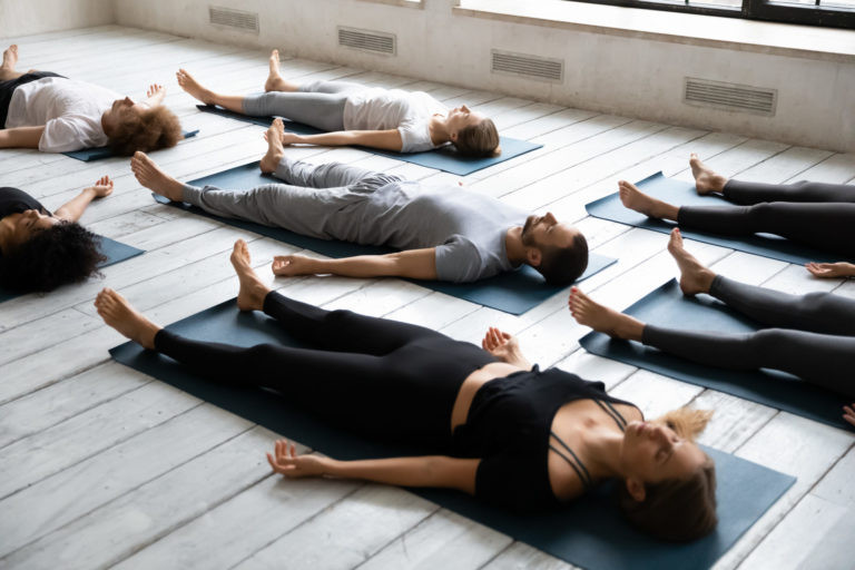 Group of young people with closed eyes meditating in Savasana pose on the floor in Salt Lake City, UT | Santosh Yoga Institute