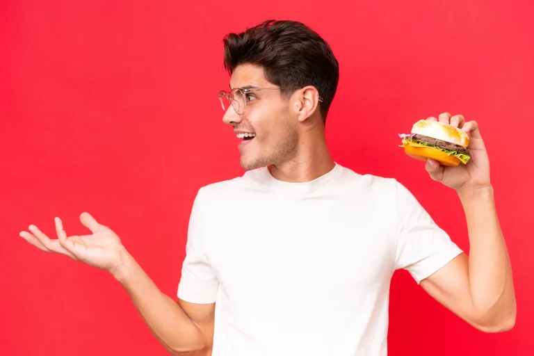 Young guy holding a burger in one hand in Salt Lake City, UT | Santosh Yoga Institute