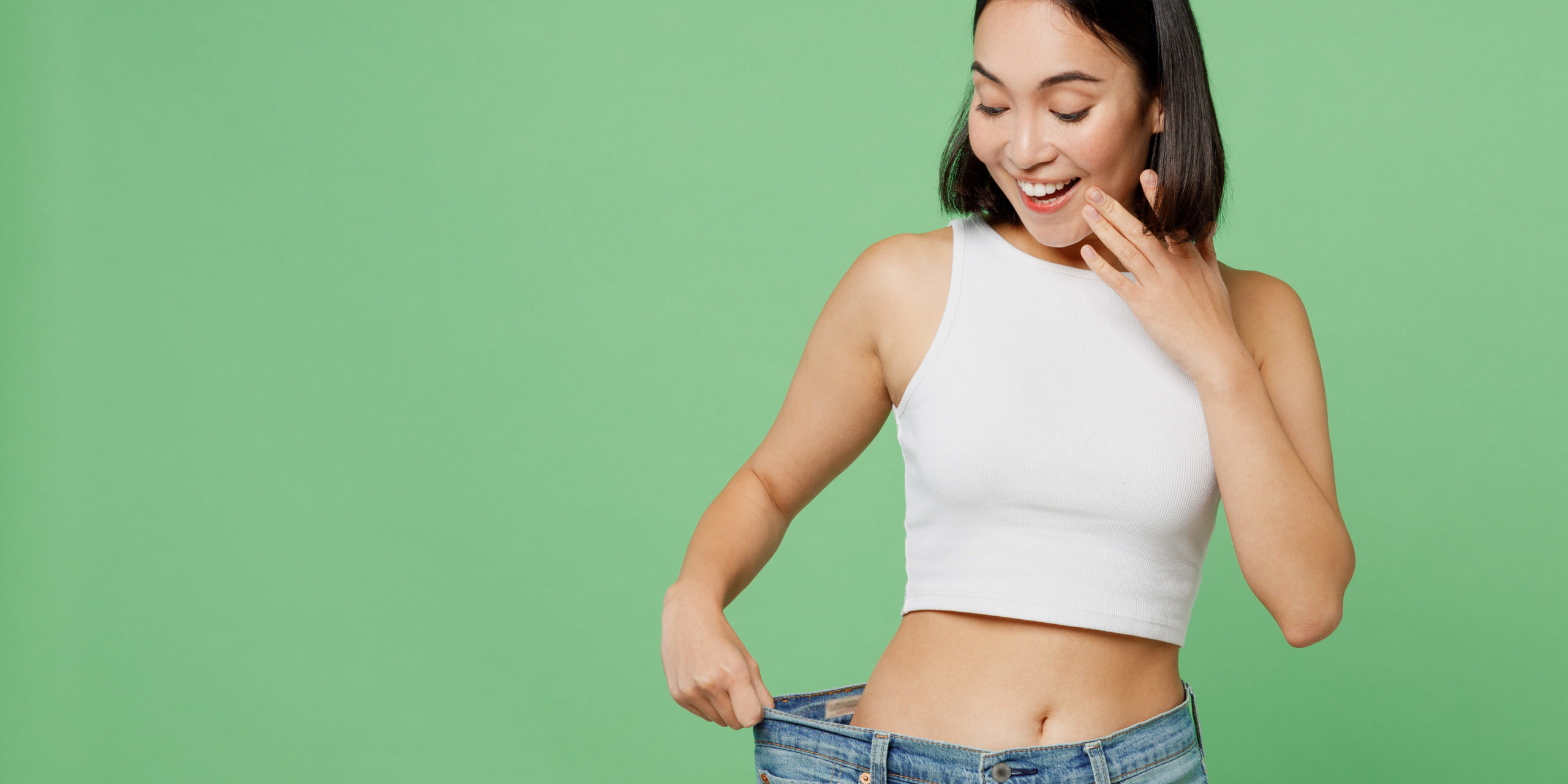 Young happy woman wears white clothes and show loose pants on waist after weight loss in Salt Lake City, UT | Santosh Yoga Institute