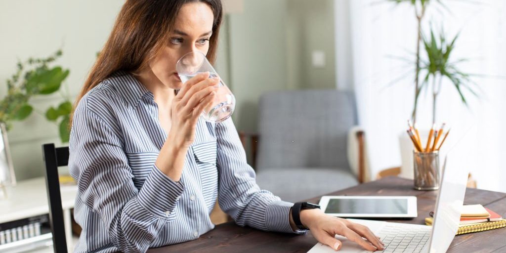 Young woman drinking a glass of water while looking at laptop in Salt Lake City, UT | Santosh Yoga Institute