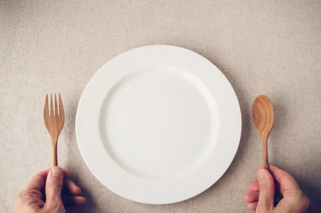 White plate on table man hands holding fork and spoon in Salt Lake City, UT | Santosh Yoga Institute