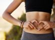 Fit young woman making a heart-shaped gesture over her stomach in Salt Lake City, UT | Santosh Yoga Institute